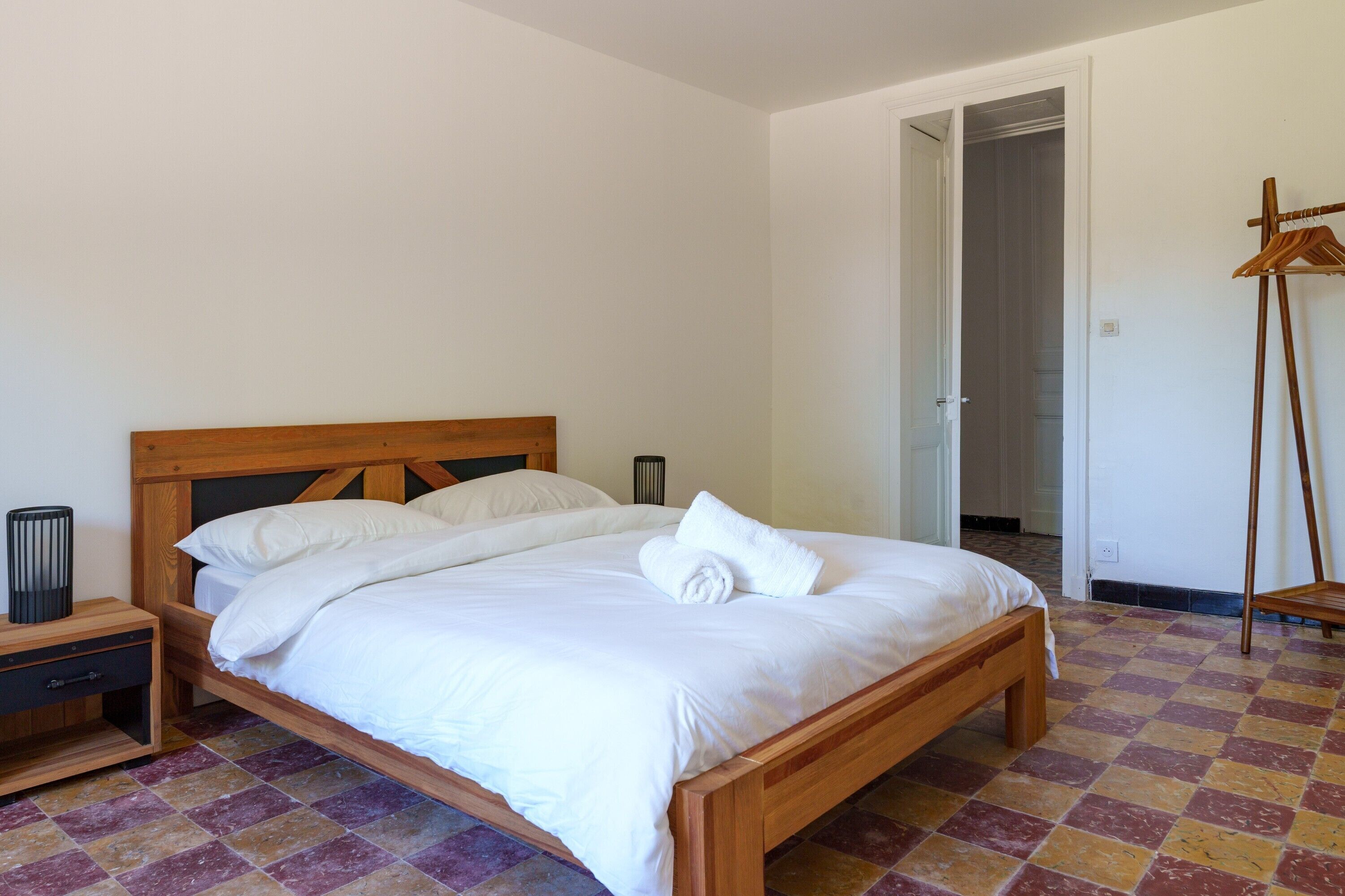 A neatly made bed with white linens, a wooden headboard, and a checkered floor.