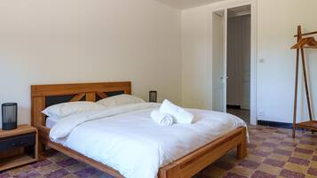A neatly made bed with white linens, a wooden headboard, and a checkered floor.