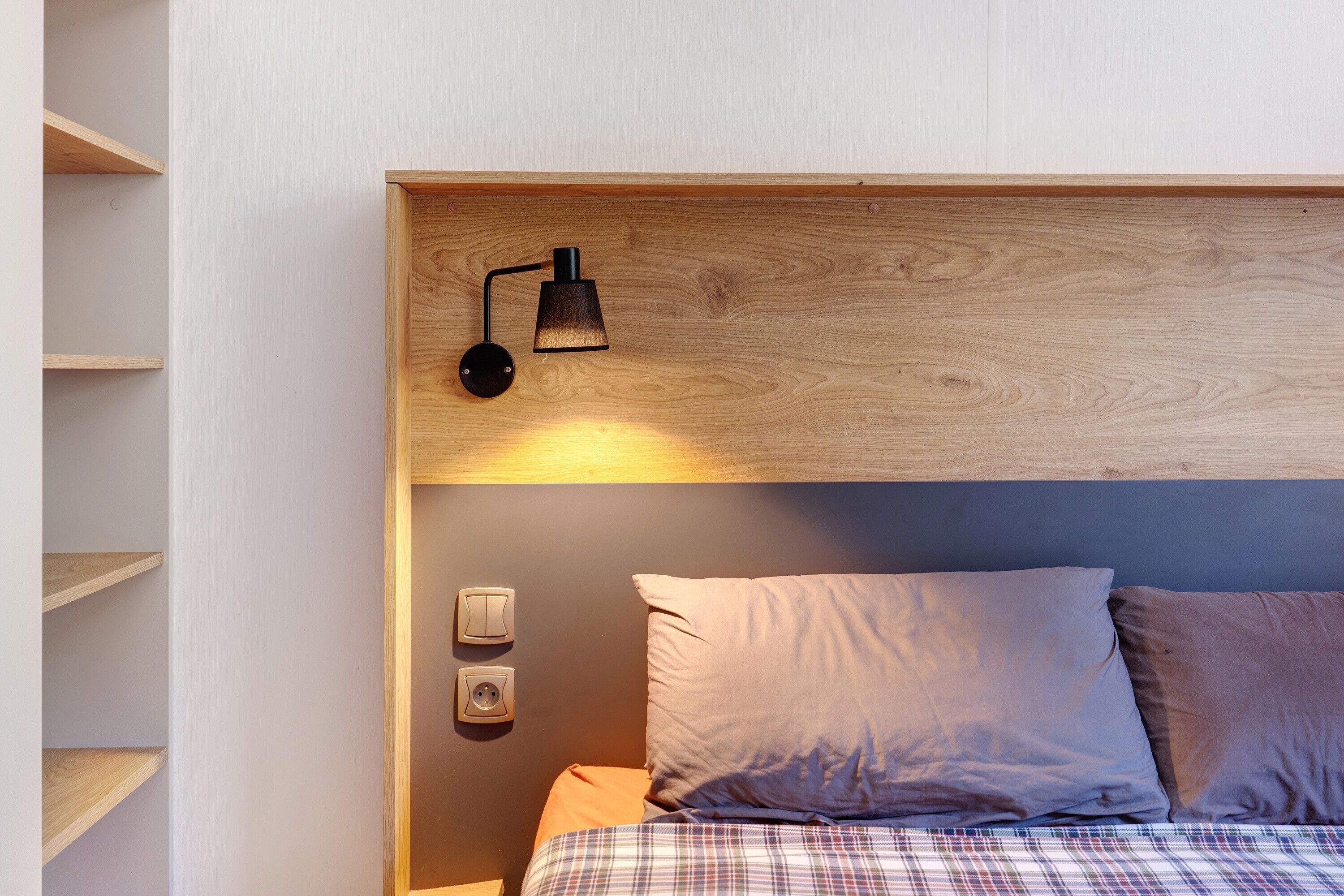 Ein Schlafzimmer mit einem hölzernen Kopfende, einem Bett mit Karomuster-Bettwäsche und einer an der Wand befestigten Lampe.