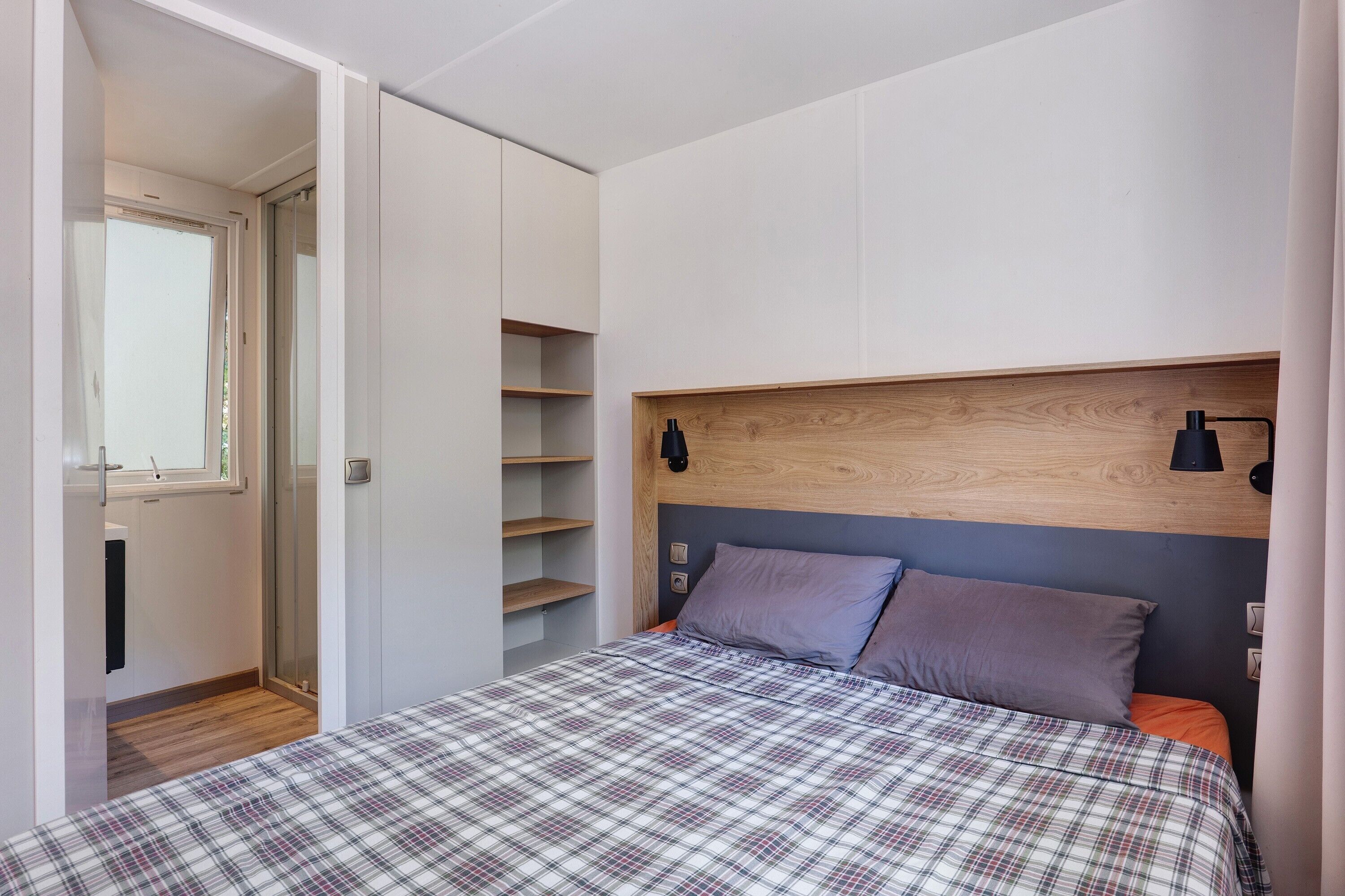 Une chambre à coucher avec un lit, une tête de lit, une table de chevet, une fenêtre et une porte.