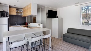 Eine moderne Küche mit weißen Schränken, ein Essbereich mit weißem Tisch und Barhocker sowie ein graues Sofa im Wohnbereich.