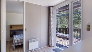 Ein Zimmer mit einem Bett, einem Heizkörper, einem Fenster mit Blick auf eine Terrasse und einer Tür zu einem anderen Raum.