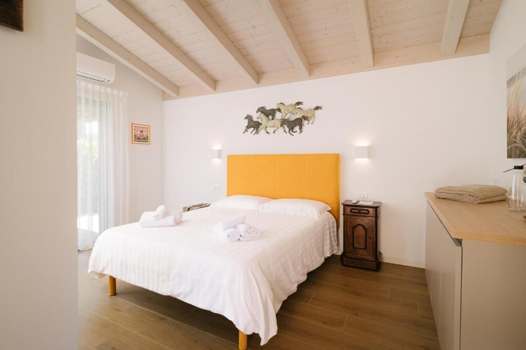 Una camera da letto con un letto, un comodino, una testiera in legno, un'opera d'arte appesa al muro e una finestra con tende.