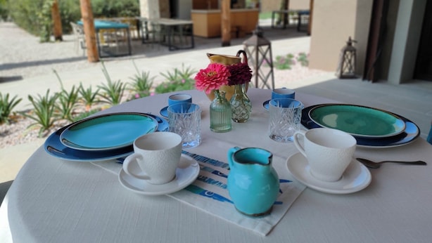 A round table set with plates, cups, and a vase with flowers, with a view of a building and greenery in the background. - Agriturismo Resort Il Foionco (Massa Marittima)