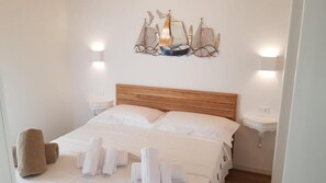 Een net opgemaakt bed met witte lakens, een houten hoofdbord en een decoratief object aan de muur erboven.