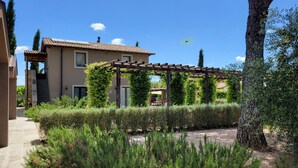 A house with a pergola, a garden with trimmed hedges, and a clear blue sky. - Agriturismo Resort Il Foionco (Massa Marittima)