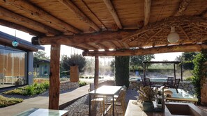 Een overdekt terras buiten met een zwembad, een houten pergola en een zithoek.