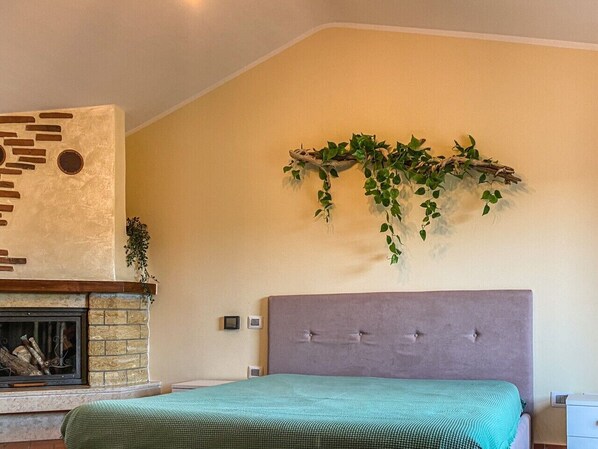 A bedroom with a fireplace, a bed with a green bedspread, a headboard, and a wall-mounted plant.