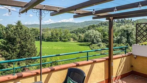 En balkon med et bord, en stol og en lygte, der udover et grønt landskab.