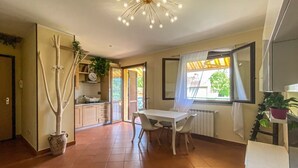 Et rummeligt værelse med spisebord, stole, en potteplante, en loftlampe og udsigt ud af et vindue.
