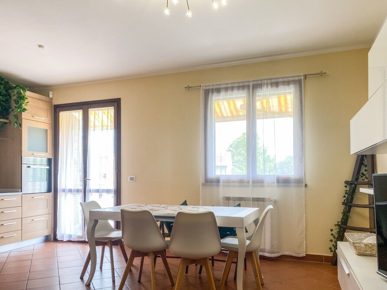 A dining area with a table and chairs, a kitchen with cabinets, and a window with curtains.