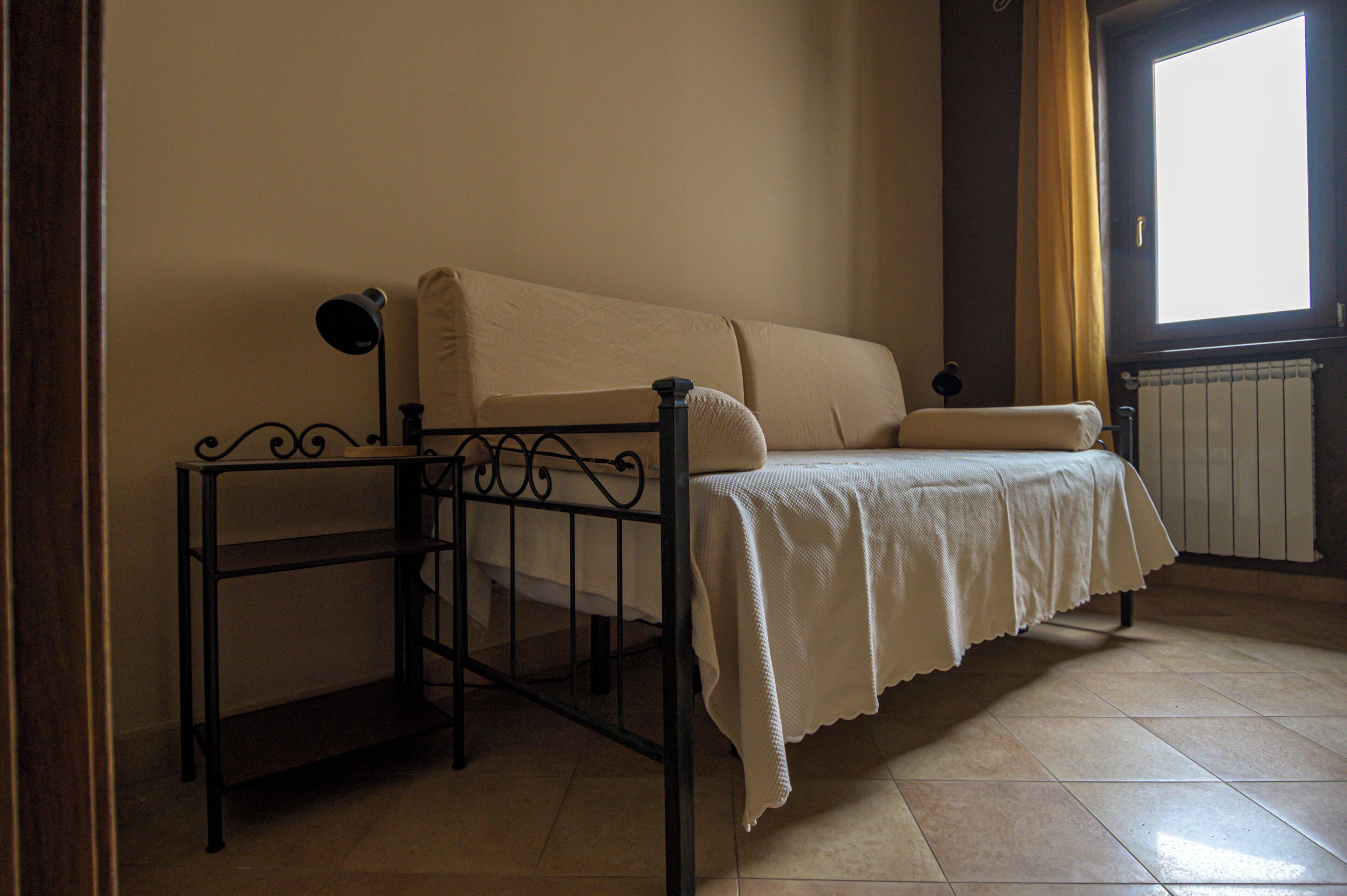 A room with a bed, a small table, a radiator, and a window with curtains.