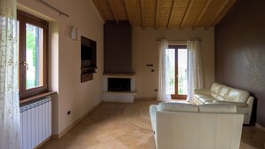 Een woonkamer met een open haard, een bank, een televisie en een raam met gordijnen.