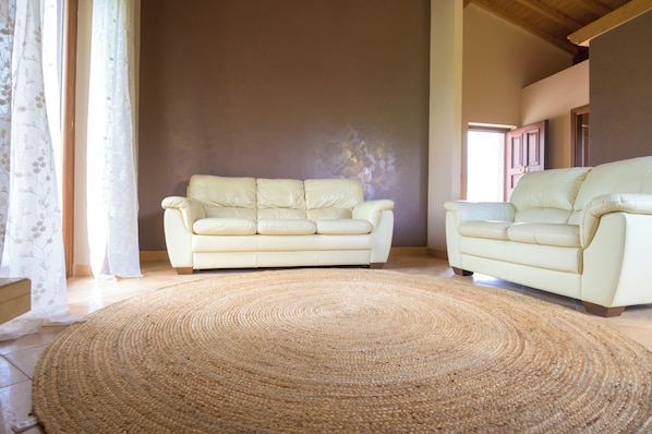 A living room with two cream-colored sofas, a woven rug, and a large window with sheer curtains.