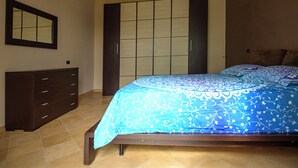 Een slaapkamer met een bed, een dressoir, een kast en een spiegel.