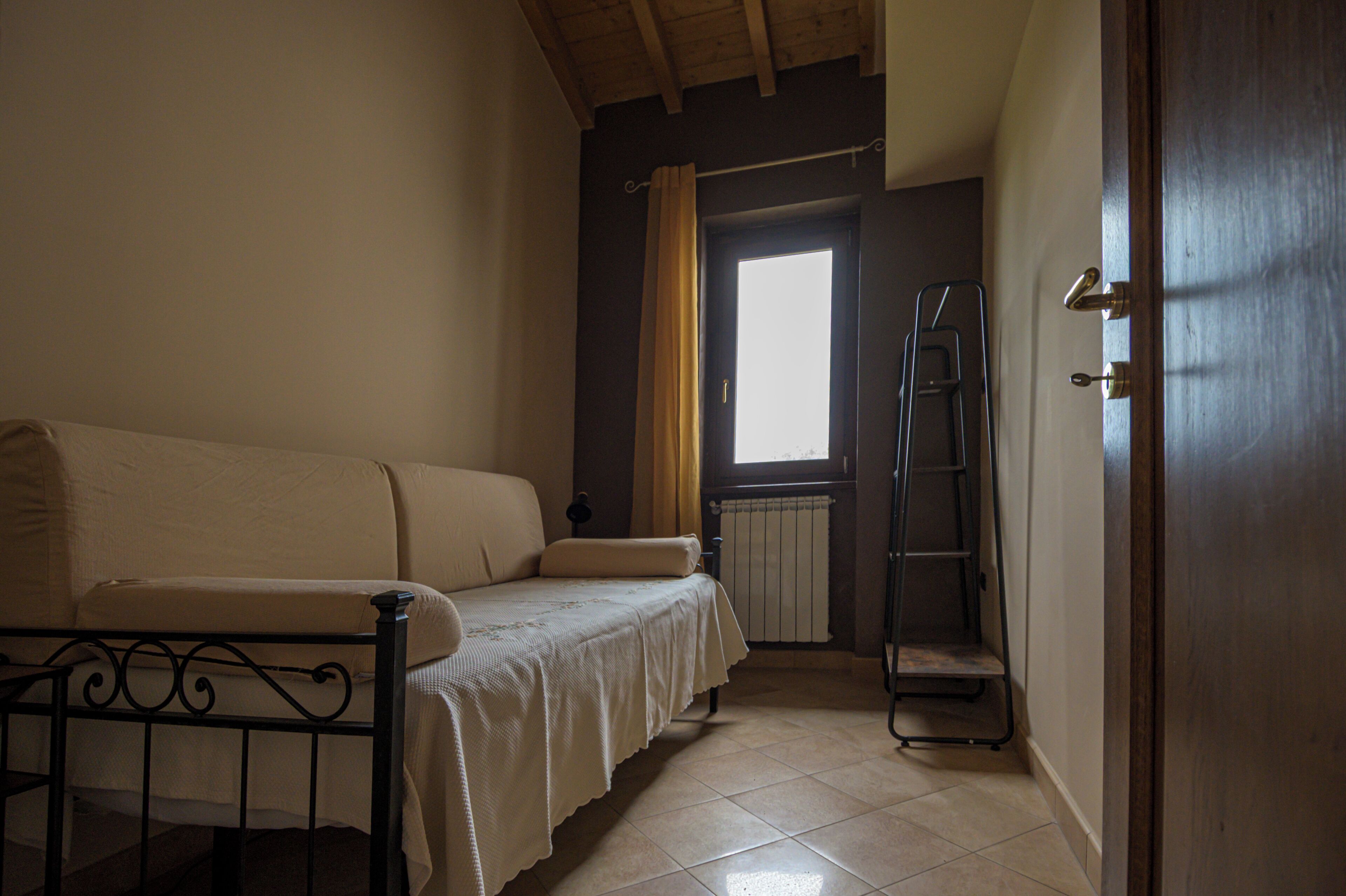 A room with a bed, a radiator, a window with curtains, a door, and a ladder.