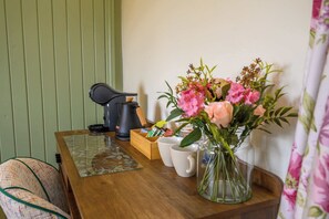 Ein Holztisch mit einer Kaffeemaschine, einer Snackbox, einer Blumenvase und einer Tasse.