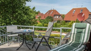 A deck with a table and chairs, a lounge chair, and a view of houses with satellite dishes. - Harleblick Carolinensiel (Wittmund)
