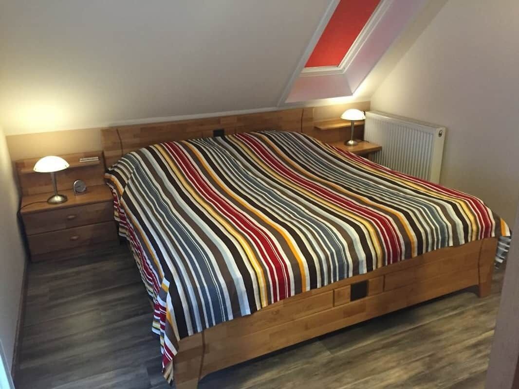 Ein Schlafzimmer mit einem hölzernen Bett, einem Nachttisch mit Lampe und einem Oberlicht über dem Bett.