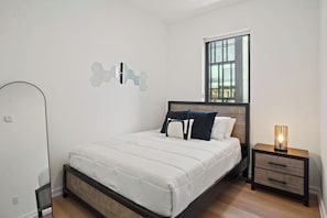 A bedroom with a bed, bedside tables, a window, and a wall-mounted light fixture.
