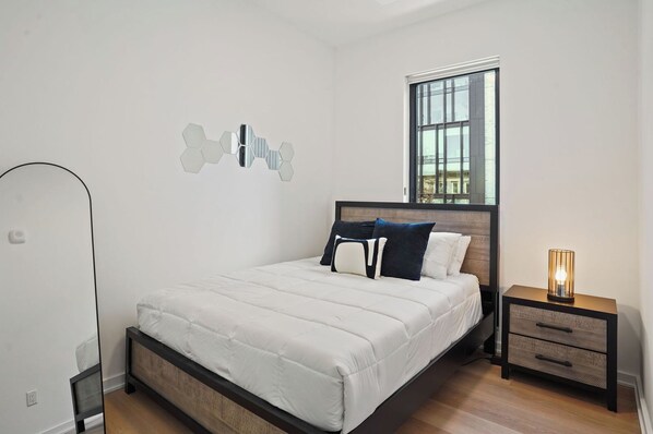A bedroom with a bed, bedside tables, a window, and a wall-mounted light fixture.