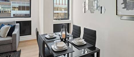 A modern dining area with a glass table, black chairs, and a view of a building with a 'PARKING' sign.