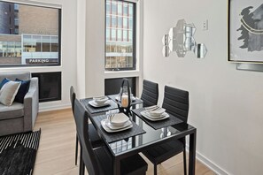 Un comedor moderno con una mesa de vidrio, sillas negras y vistas a un edificio con un cartel de 'PARKING'.