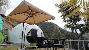 A tent with a hanging chair, a table with chairs, and a white fence. - Manzil Escapes (Dhanaulti)