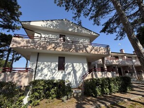 Ein mehrgeschossiges Gebäude mit flachem Dach, einem Balkon im oberen Geschoss und einer Treppe, die zum Eingang führt.