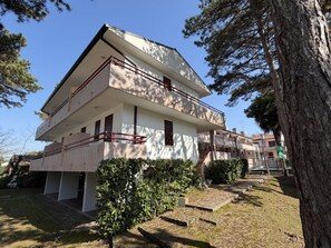 Ein zweistöckiges Gebäude mit Balkon, umgeben von Bäumen und einer Rasenfläche.