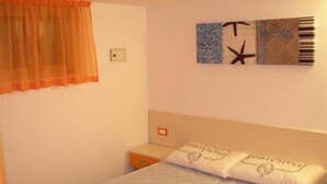 Een slaapkamer met een bed, nachtkastje, wandklok en een raam met gordijnen.