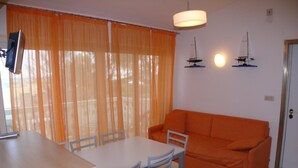 Een zithoek met een tafel, stoelen, een oranje bank en twee decoraties van zeilboten aan de muur.
