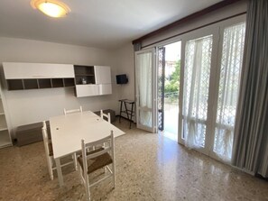 Ein Zimmer mit weißem Tisch und Stühlen, einer eingebauten Regaleinheit, einem Fernseher und einer Glastür zum Außenbereich.