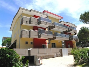 Ein mehrstöckiges Gebäude mit Balkonen, einer flachen Dachterrasse und einem verschlossenen Eingang.