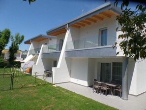 Ein modernes, zweigeschossiges Haus mit Flachdach, großen Fenstern und einer Terrasse mit Gartenmöbeln.
