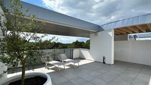 En moderne udendørs terrasse med en hvid væg, et træ og et siddeområde.