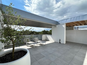 Eine moderne Außenpatio mit weißer Wand, einem Baum und einer Sitzgelegenheit.