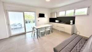 Et moderne køkken med spiseplads, et fladskærms-tv og en skydedør, der fører ud til en udendørs terrasse.