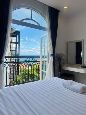 Hotellihuone, jossa on sänky, tuuletin, peili ja suuri ikkuna, josta avautuu näkymä merelle.