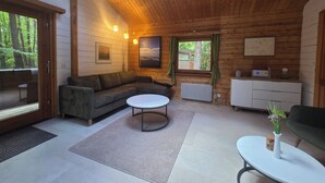 A cozy cabin interior with a sectional sofa, a round coffee table, a small white table, a cabinet, and a window with curtains. - Idyllic wooden house on the Steinhuder Meer (Neustadt am Rübenberge)