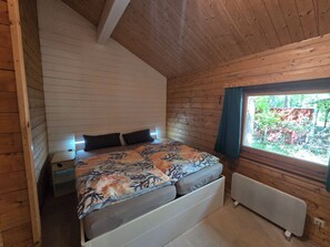 Una habitación con paneles de madera, una cama, una mesita de noche, una ventana con vistas a zonas verdes y un radiador.
