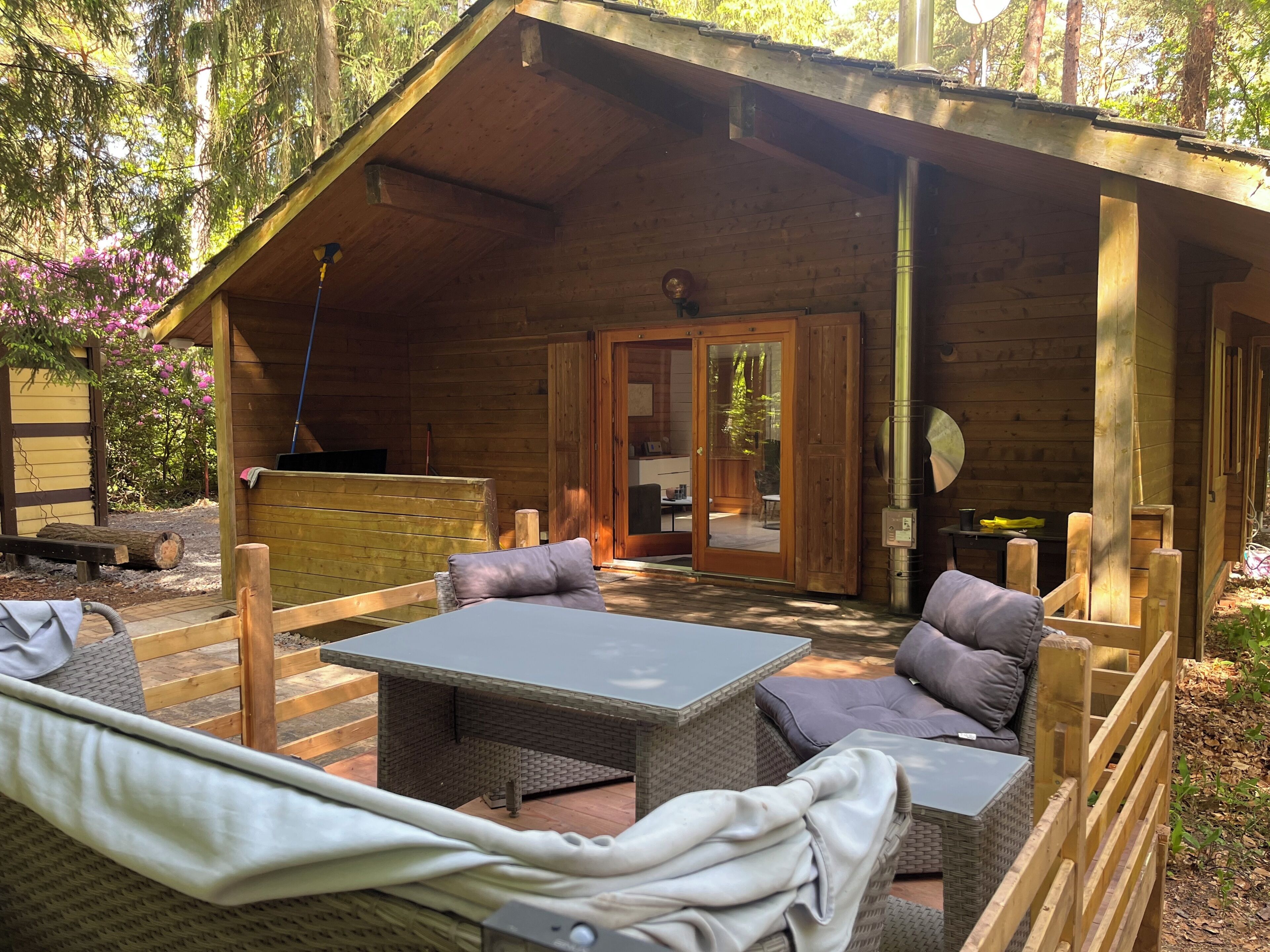 Una cabaña de madera con un área de patio que cuenta con una mesa y sillas, una terraza de madera y una puerta que da a un espacio interior.