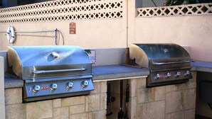 Duas grelhas a gás de aço inoxidável com botões de controlo, uma mangueira e um flutuador, tudo sobre uma bancada em azulejo.