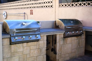 Zwei Edelstahl-Gasgrills mit Drehreglern, ein Schlauch und ein Rettungsring auf einer gefliesten Arbeitsplatte.