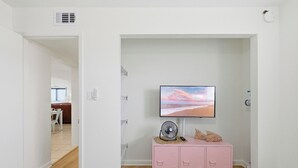 Um quarto com televisão fixada na parede, um armário rosa com gavetas e chão de madeira.