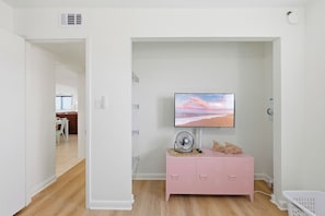 Ein Zimmer mit an der Wand montiertem Fernseher, einem pinken Schrank mit Schubladen und Holzboden.