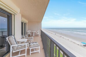 A balcony with white furniture, a view of the beach, and a clear sky. - 2 Bedroom Corner Oceanfront (New Smyrna Beach)