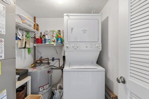 Ein kleiner Hauswirtschaftsraum mit einer Waschmaschine mit Frontlader, einem Trockner und verschiedenen Reinigungsmitteln auf Regalen.