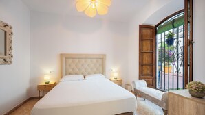 Un dormitorio con una cama grande, lámparas de noche, un banco, cabecera de madera, un espejo y una ventana con vistas al exterior.