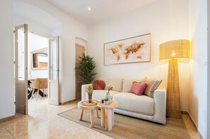 Ein Wohnzimmer mit einer Couch, zwei Beistelltischen, einer Lampe und einem großen abstrakten Gemälde an der Wand.